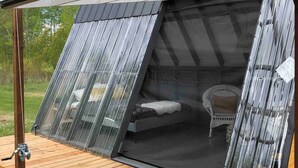Un espace de couchage extérieur moderne, doté d’une terrasse en bois, d’un lit et d’une chaise.