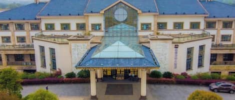 Un grand bâtiment au centre, doté d’une structure distinctive en verre et en métal, entouré d’un espace paysager agrémenté de sentiers et de verdure.