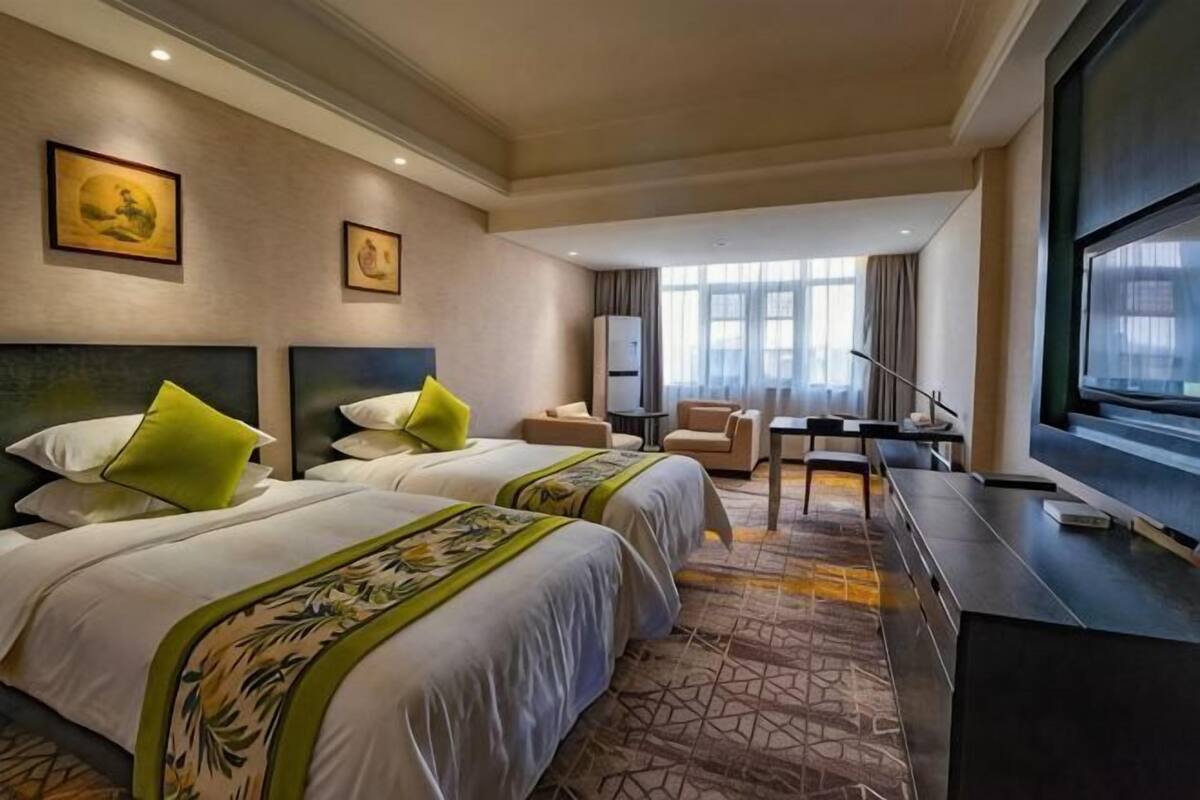 A hotel room with two beds, a desk, a chair, a TV, and a large window.