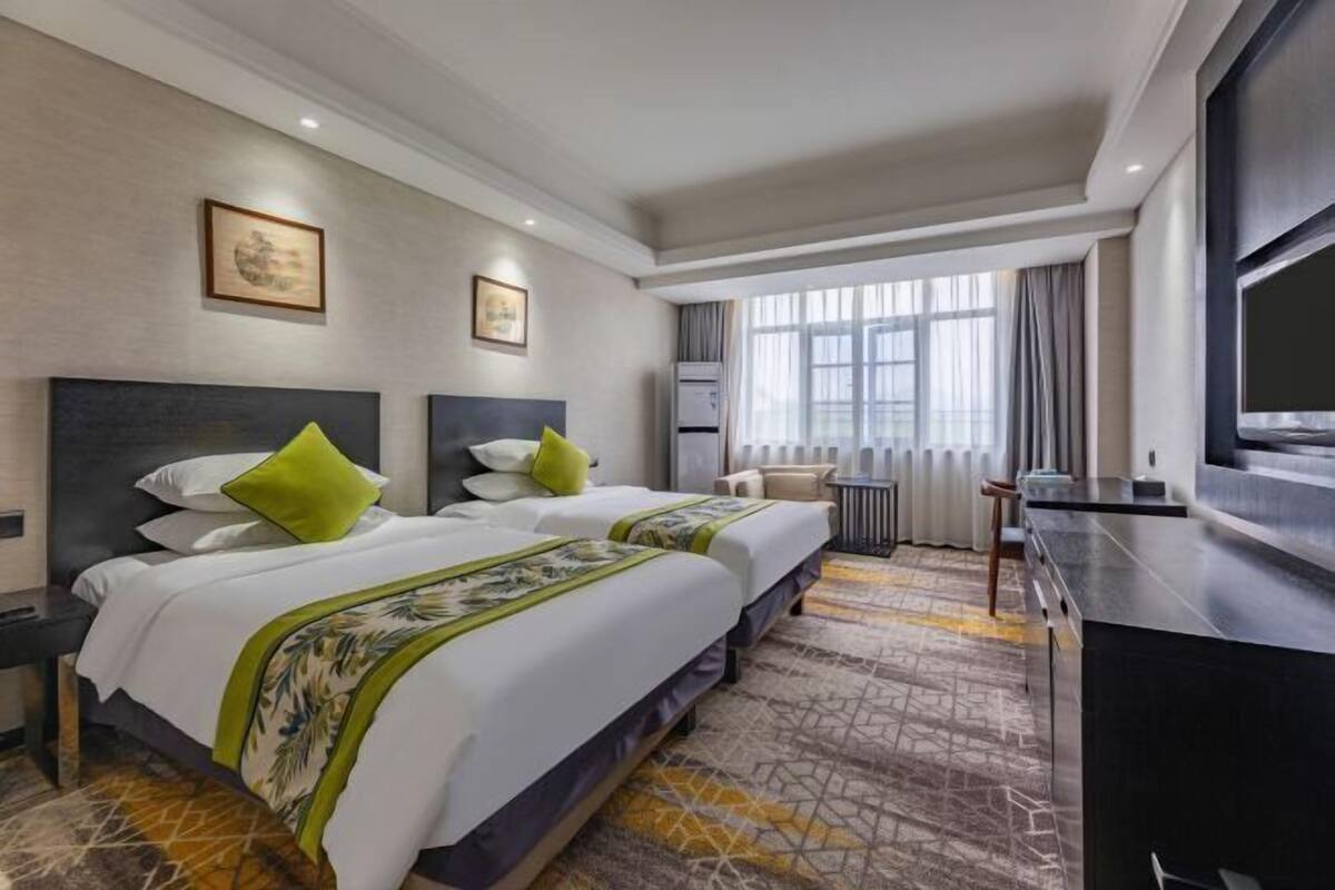A hotel room with two beds, a TV, a desk, and a window with curtains.