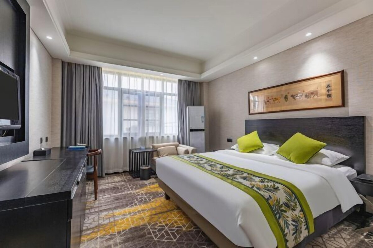 A hotel room with a bed, a desk, a chair, a television, and a window with curtains.