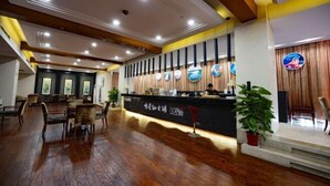 A reception area with a wooden floor, a reception desk, and a seating area with chairs. - Metropark Longhua Hotel (Xinyu)
