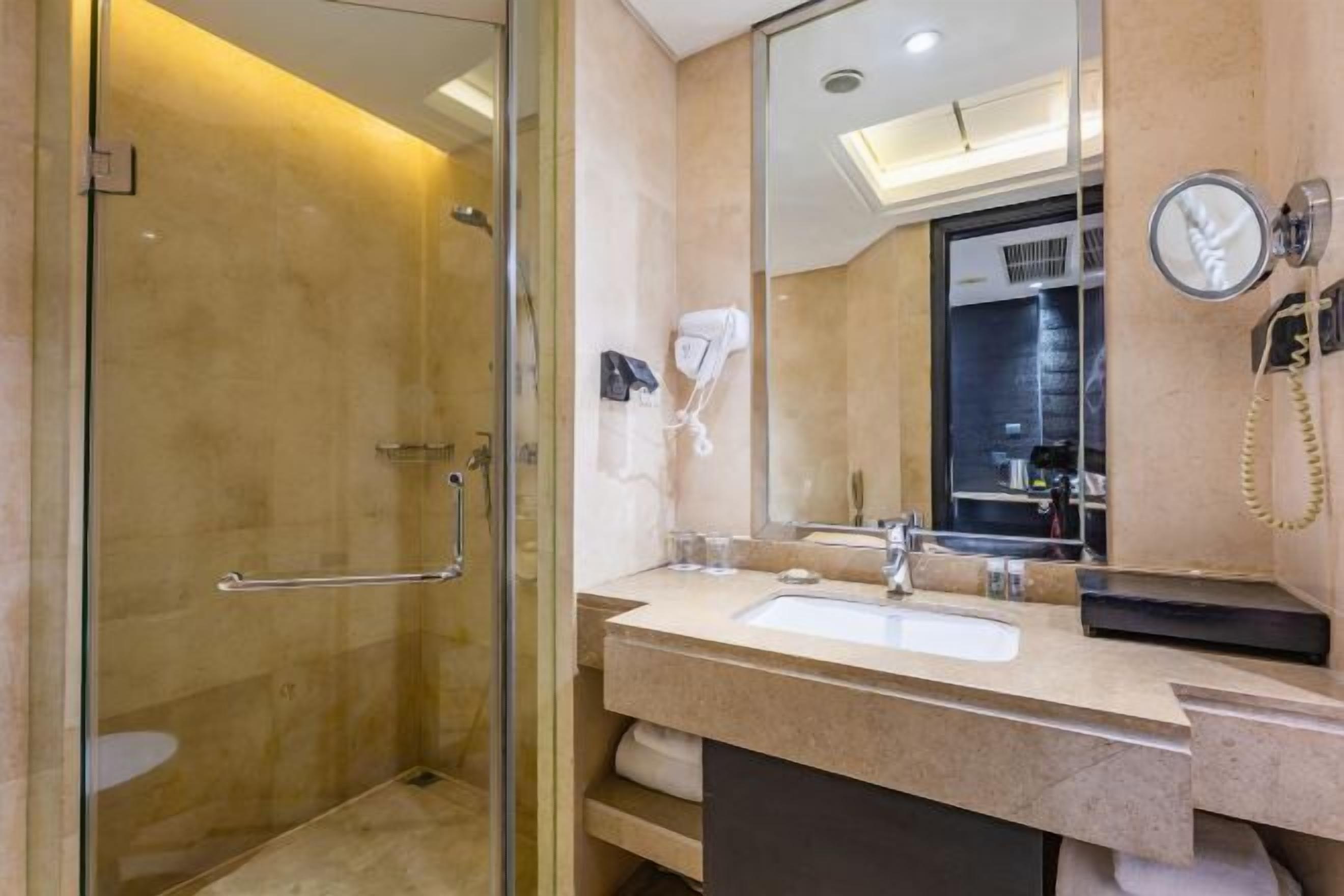 Een moderne badkamer met een douchecabine, een wastafel met spiegel en een aan de muur bevestigde haardroger.
