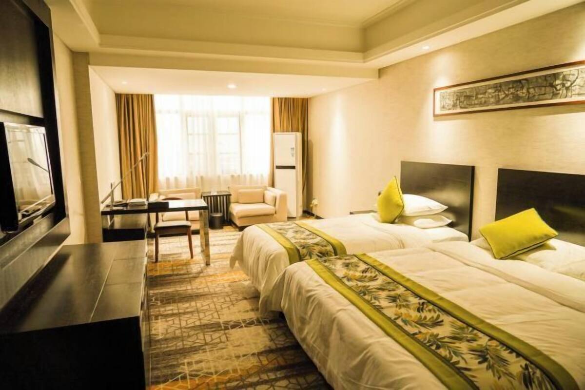 A hotel room with two beds, a desk, a chair, a television, and a window with curtains.