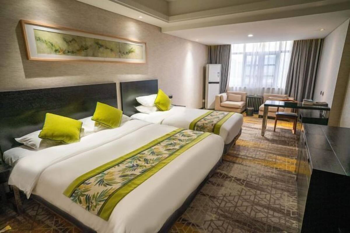 A hotel room with two beds, a desk, a chair, and a large window.