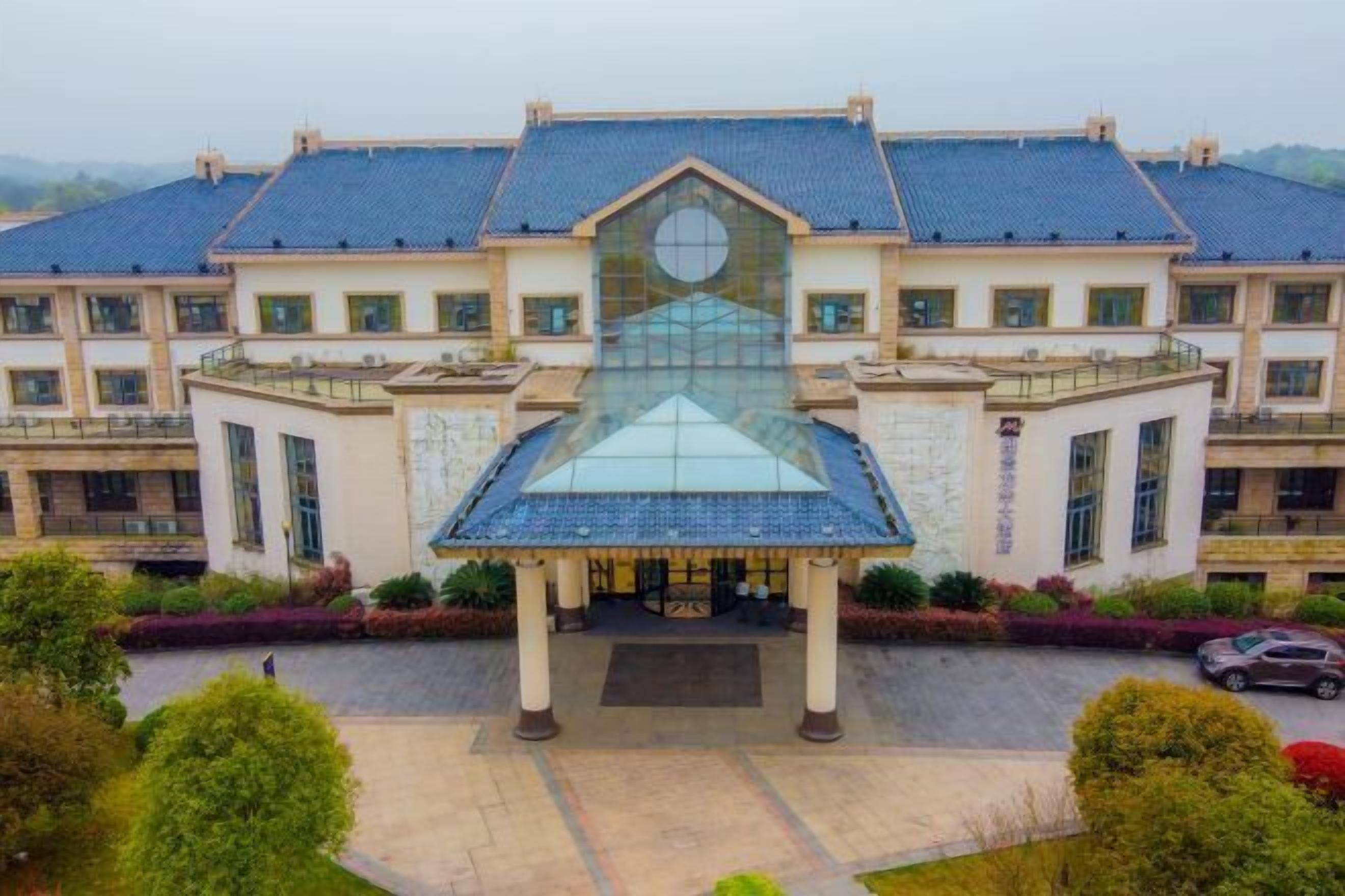 Un grand bâtiment doté d’une façade centrale en verre et d’une toiture à symétrie parfaite.