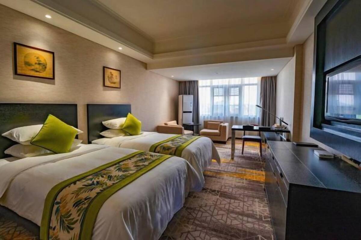 A hotel room with two beds, a desk, a chair, a television, and artwork on the walls.