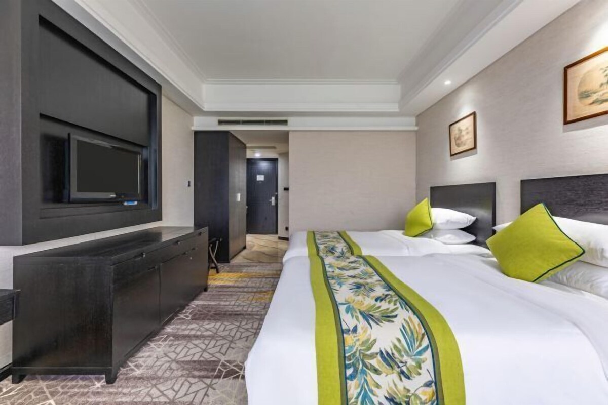 A hotel room with a large bed, a flat-screen TV mounted on the wall, a dark wooden dresser, and a carpeted floor.