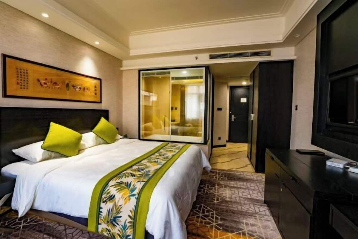 A hotel room with a large bed, a television, a sliding door, and a framed artwork on the wall.