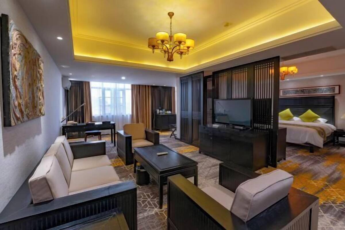 A hotel room with a sofa, armchairs, a TV, a piano, and a bed with a headboard.