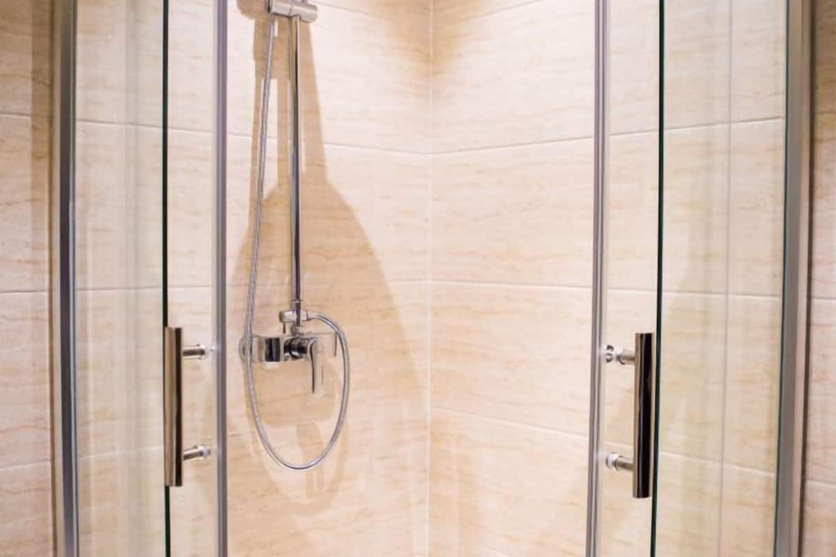 A glass-enclosed shower with a handheld showerhead and a control panel.