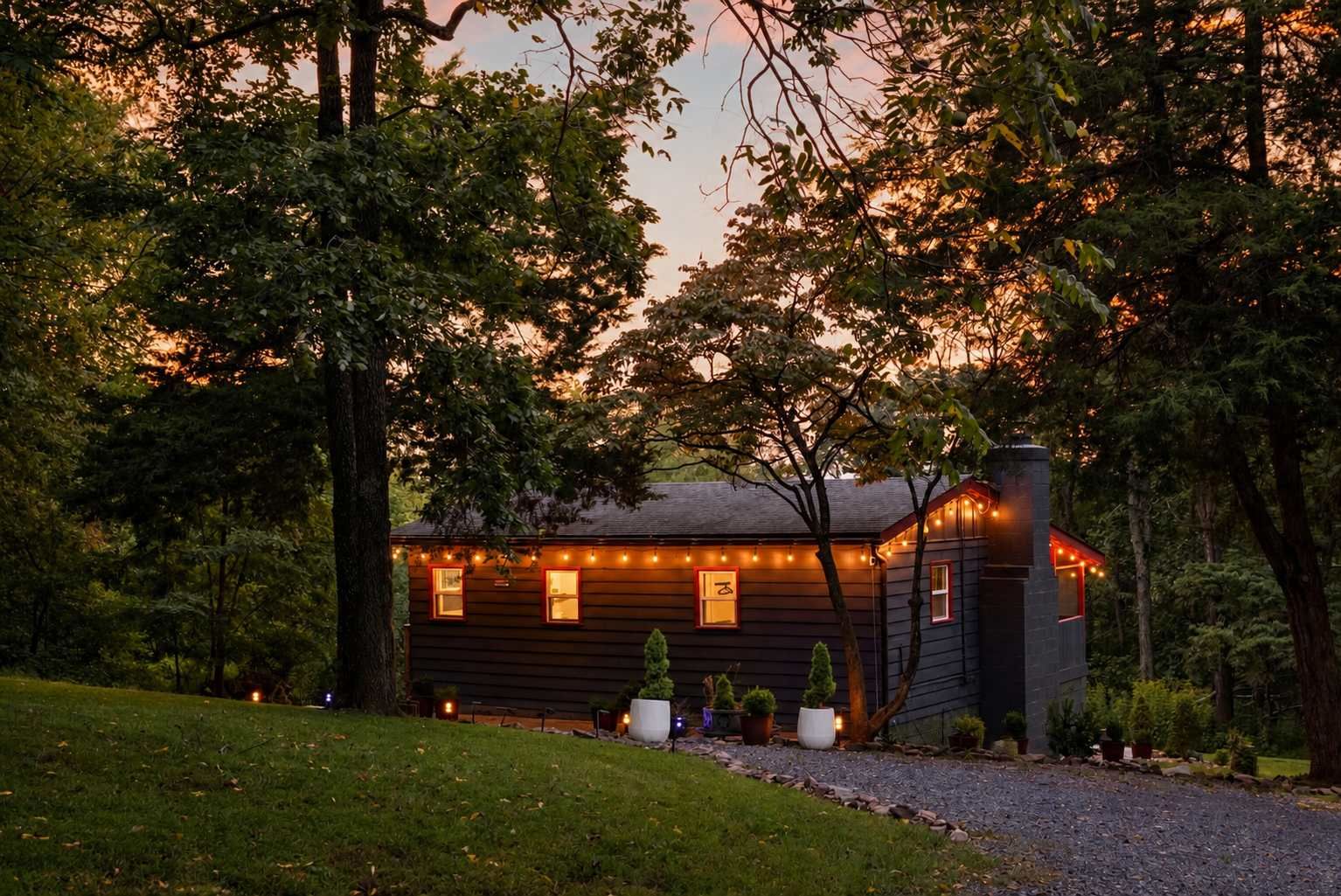 A cabin with a gravel driveway, surrounded by trees and potted plants.