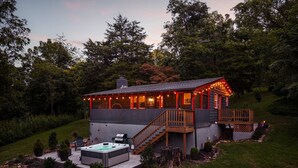 A house with a deck, outdoor hot tub, and a staircase leading to a covered porch.