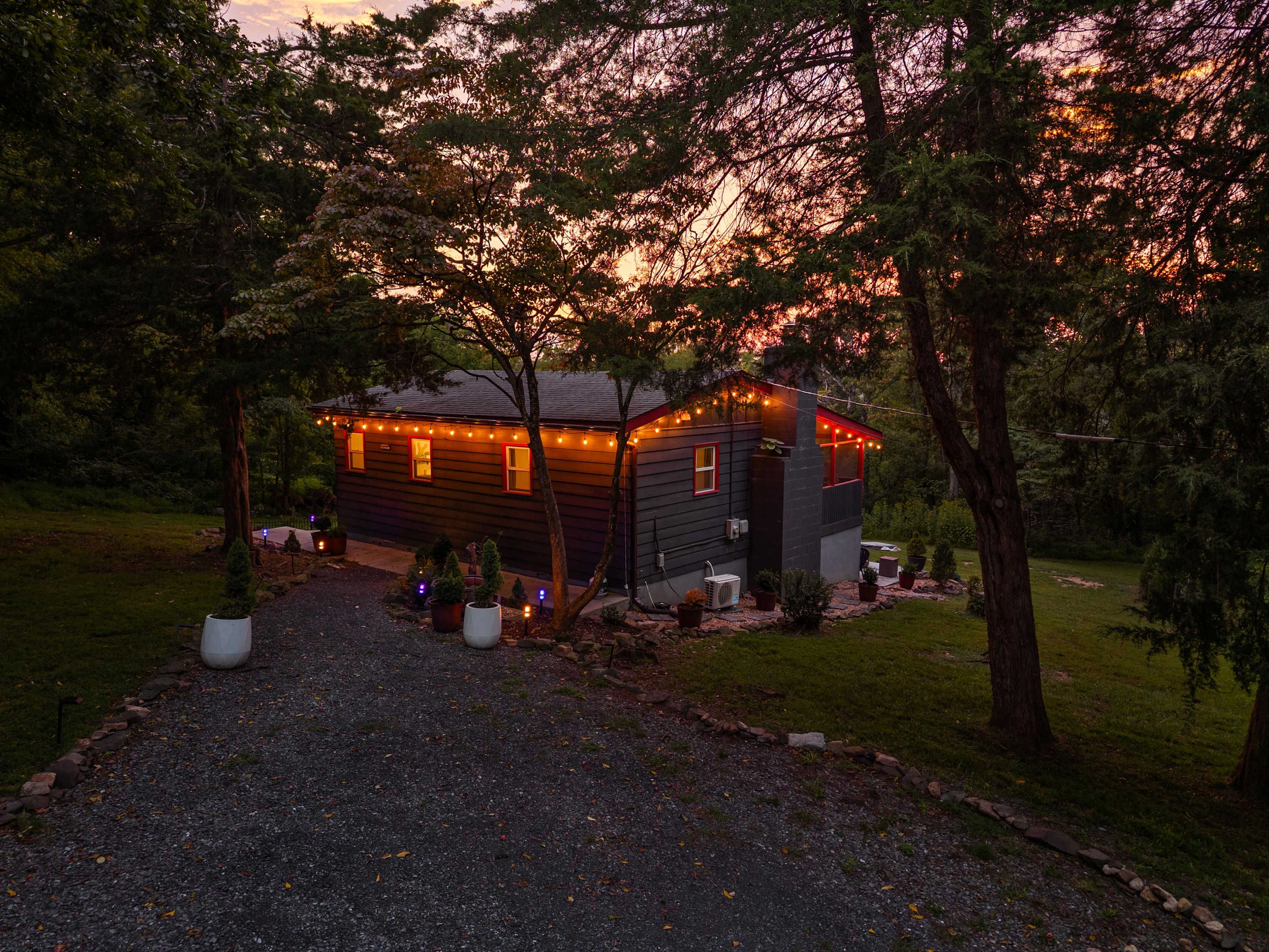 A cabin with a gravel driveway, surrounded by trees and potted plants.