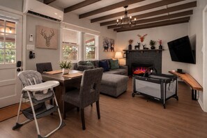 A living room with a fireplace, a television, and a dining area with a high chair. - The Juniper Cabin | Cozy Hideaway w/ Hot Tub, Screened Porch + Fire Pit (Linden)