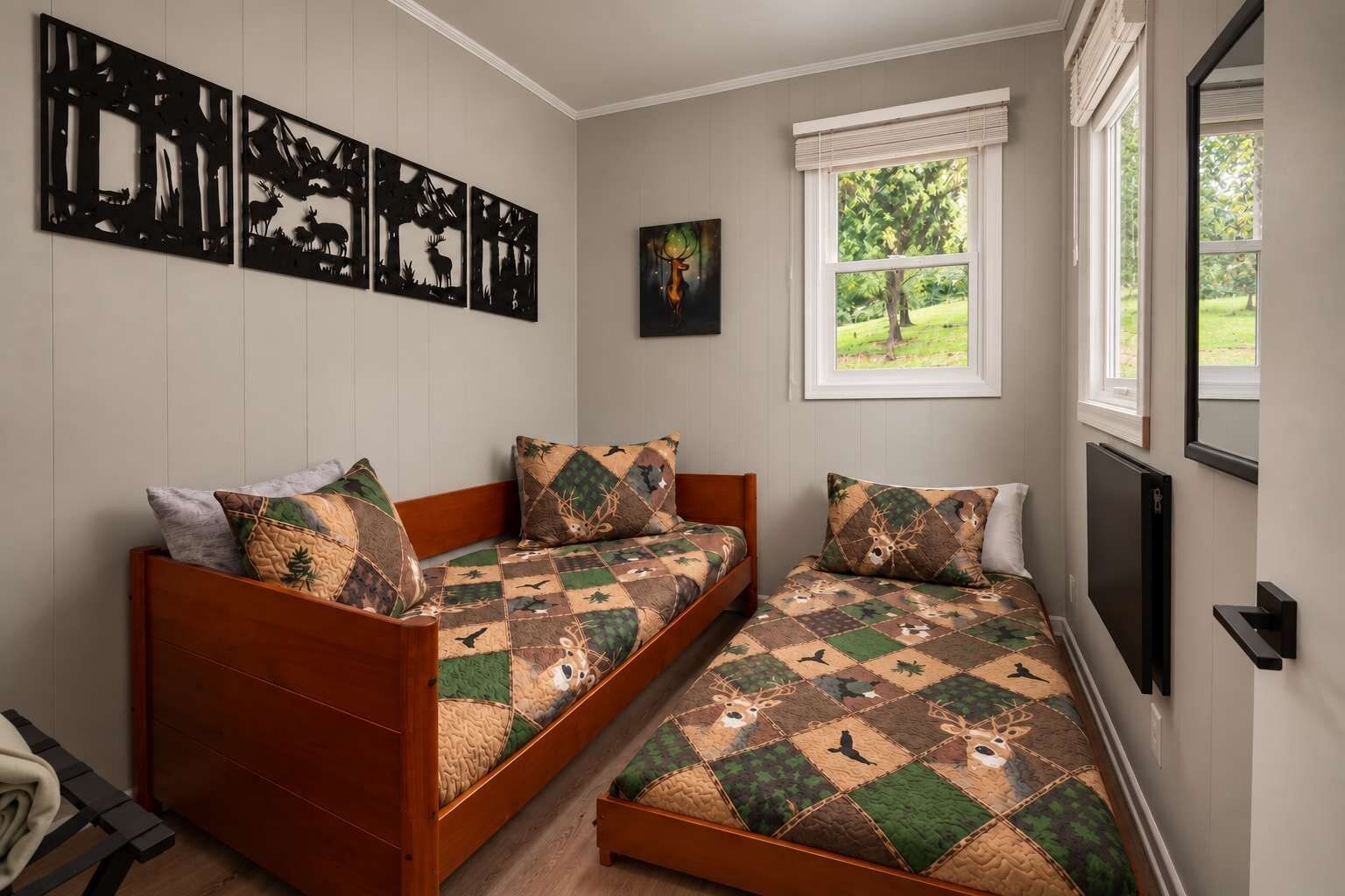 Ein Zimmer mit zwei Holzbetten, einem Fenster mit Blick auf Grünflächen und Wandbildern, die Wildtiere zeigen.