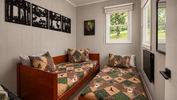 Une chambre avec deux lits en bois, une fenêtre donnant sur un paysage verdoyant et des œuvres d’art murales représentant des animaux sauvages.