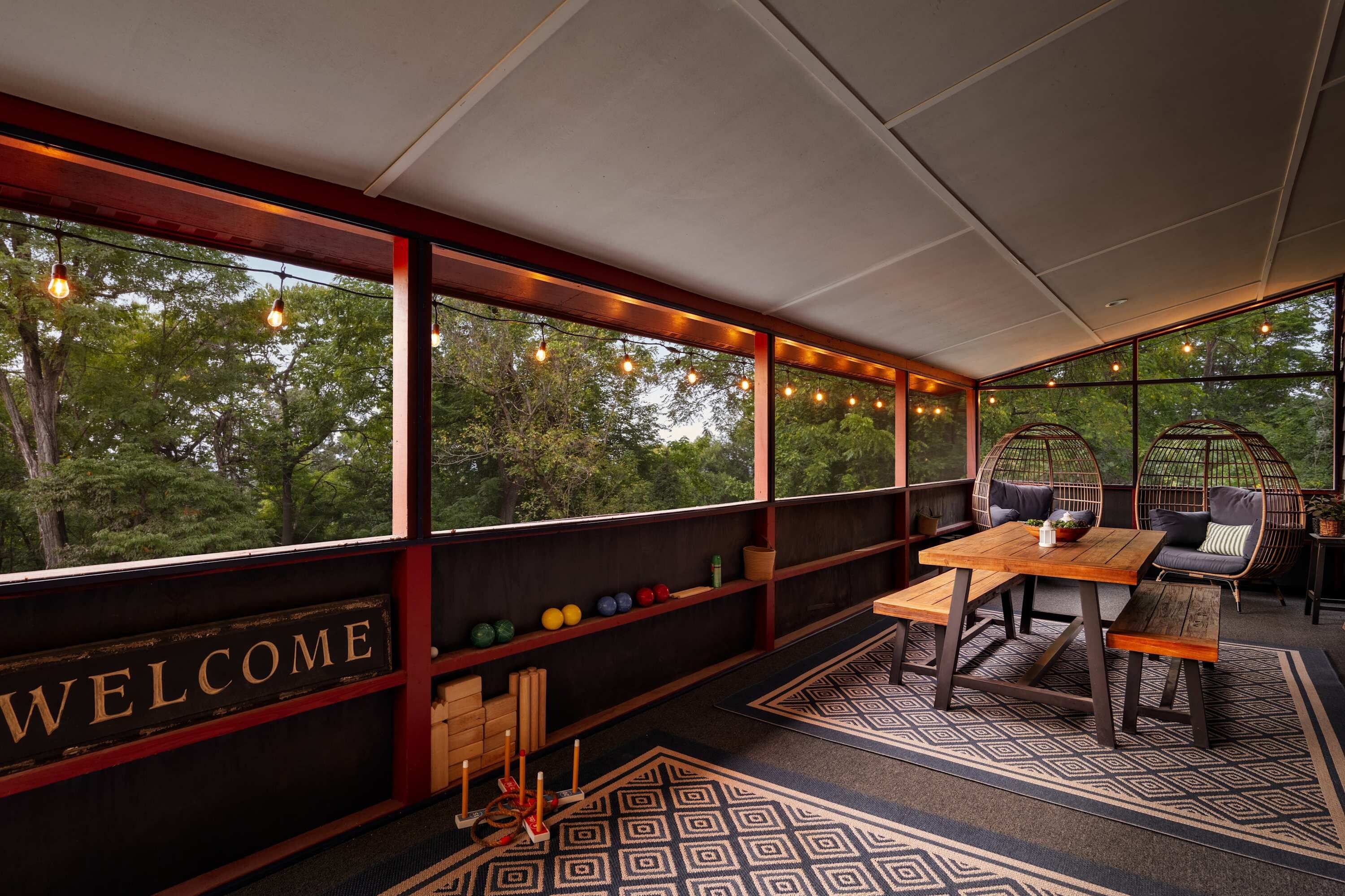 A cozy outdoor seating area with a 'WELCOME' sign, wooden furniture, and a patterned rug.