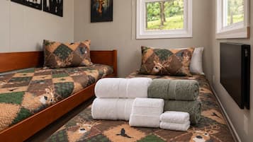 A room with a bed featuring a deer-themed quilt, a window with a view of trees, and a flat-screen TV mounted on the wall.