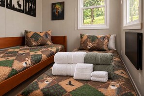 A room with a bed featuring a deer-themed quilt, a window with a view of trees, and a flat-screen TV mounted on the wall.