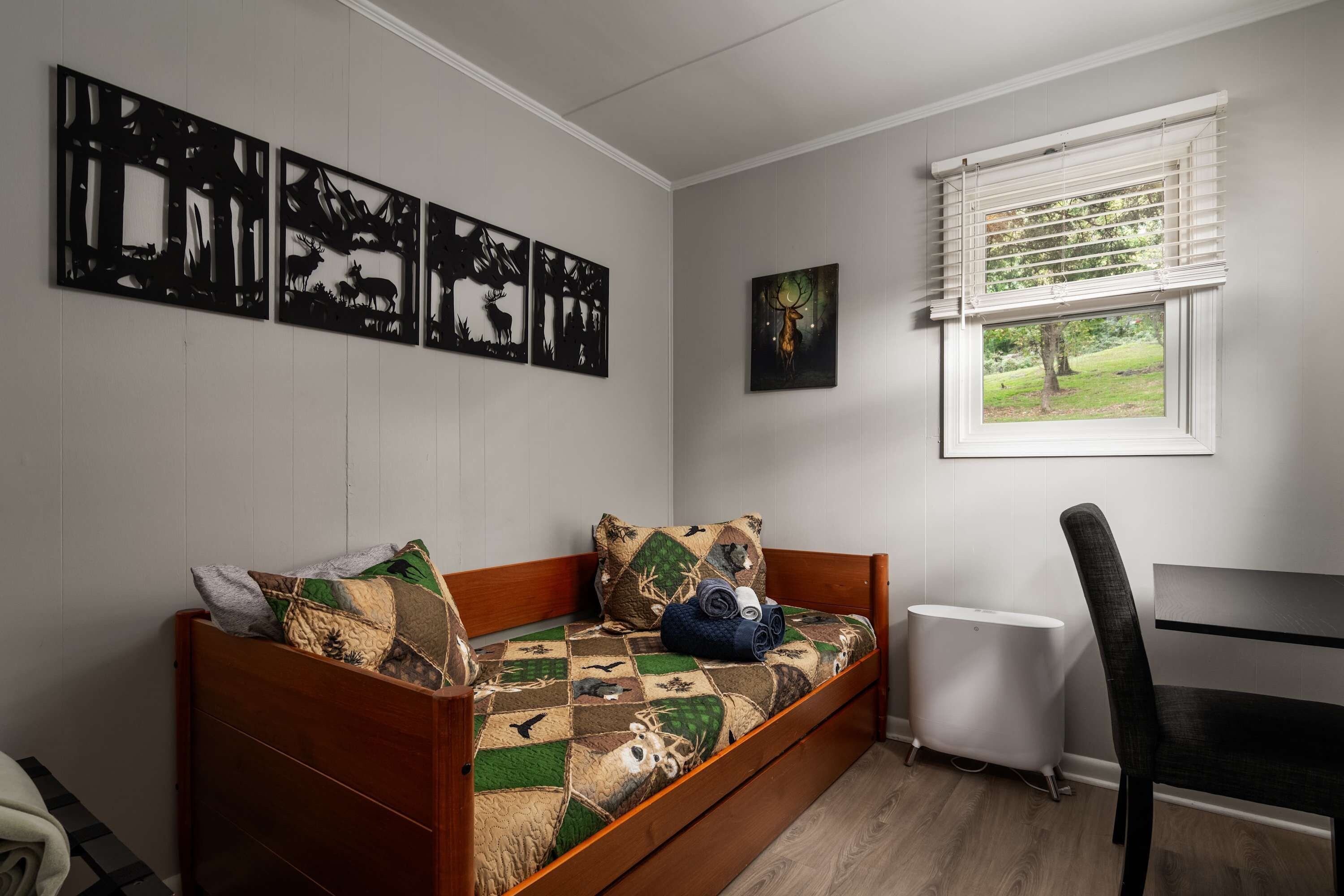 A room with a wooden sofa bed, a window with blinds, a radiator, and wall art depicting deer.