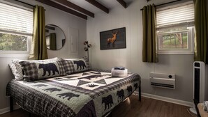 A bedroom with a bed, a mirror, a wall-mounted deer picture, a radiator, and a window with curtains.