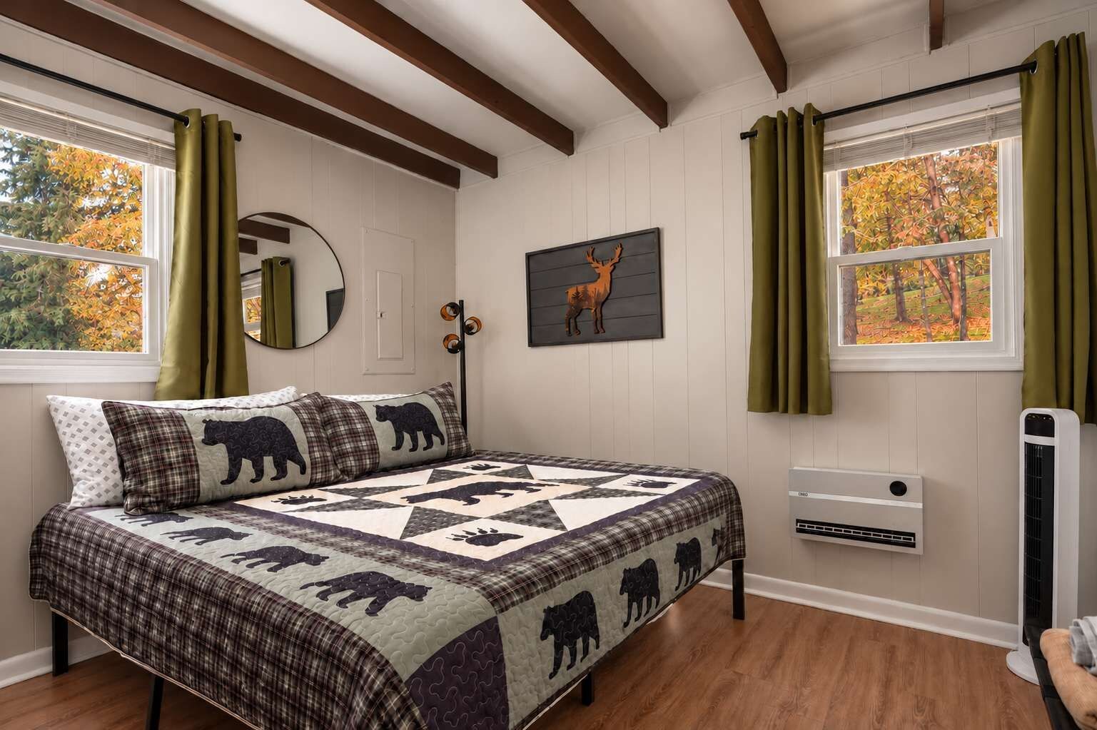 The king bedroom has windows on two sides, a bear-print quilt, and a view of green trees from bed.