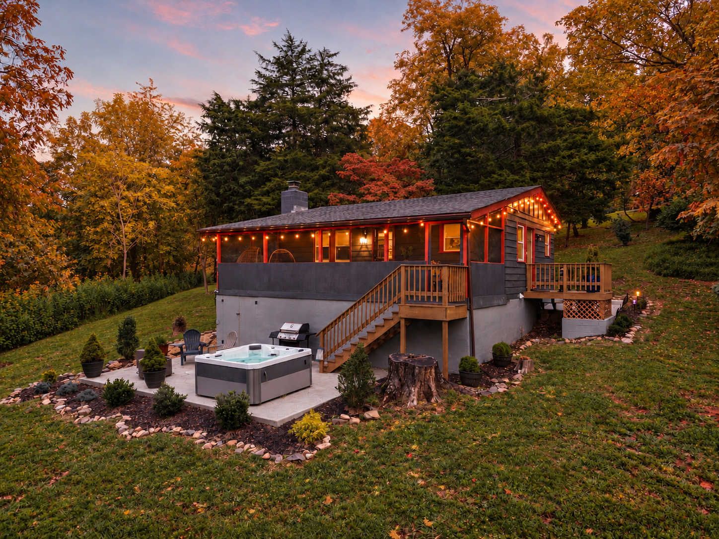 The Juniper Cabin at dusk, with string lights along the porch and the hot tub ready on the patio below.