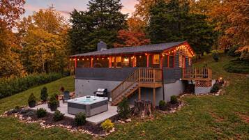 The Juniper Cabin at dusk, with string lights along the porch and the hot tub ready on the patio below.