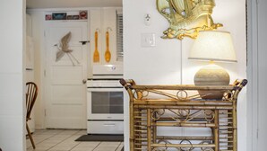 A kitchen with white cabinets, a stove, and a wicker chair. - Downtown Cottage! Walk/Cart Everywhere, 2 King Beds (Ocean Springs)