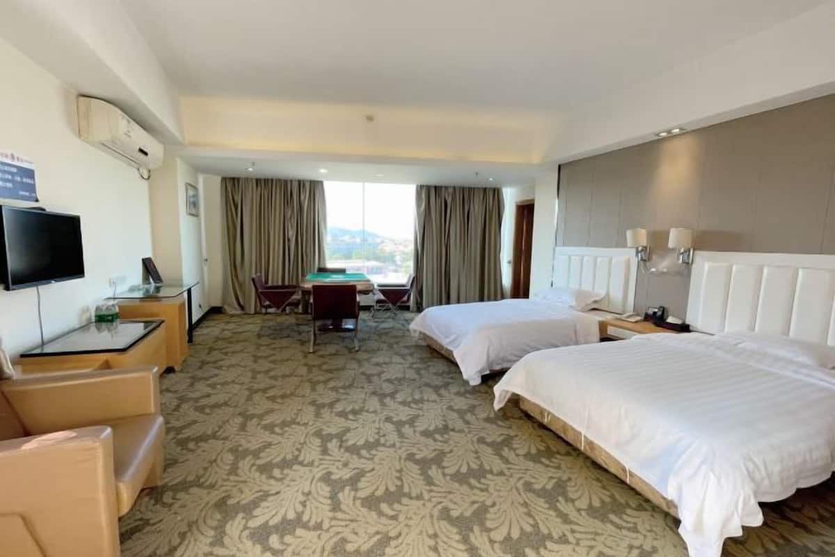 A hotel room with two beds, a desk, a chair, a television, and a view of the outdoors.