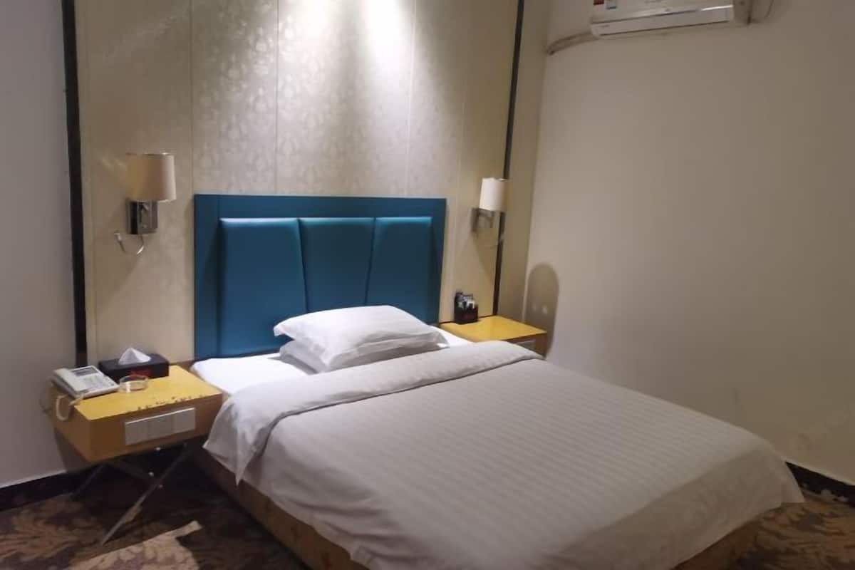 A hotel room with a single bed, a bedside table, a lamp, and a wall-mounted air conditioner.
