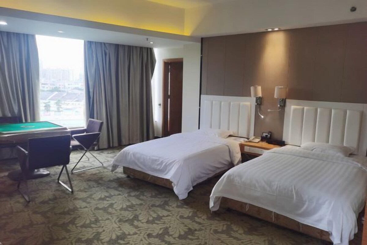 A hotel room with two beds, a desk with a pool table, and a view of the city.