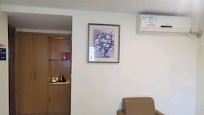A room with a beige armchair, a framed floral artwork on the wall, a wooden wardrobe, and an air conditioning unit. - Jufu Hotel (Enping)