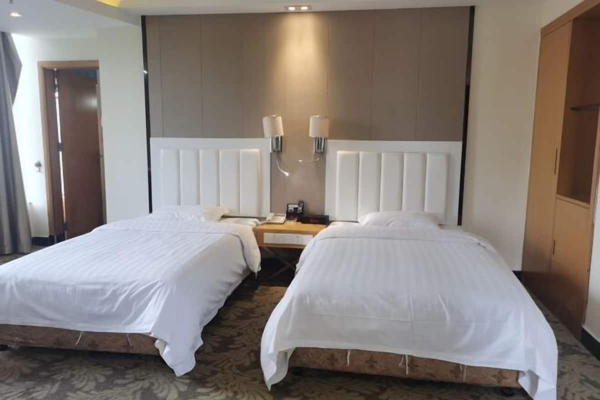A hotel room with two beds, a wooden headboard, a nightstand with a lamp, and a door to the left.