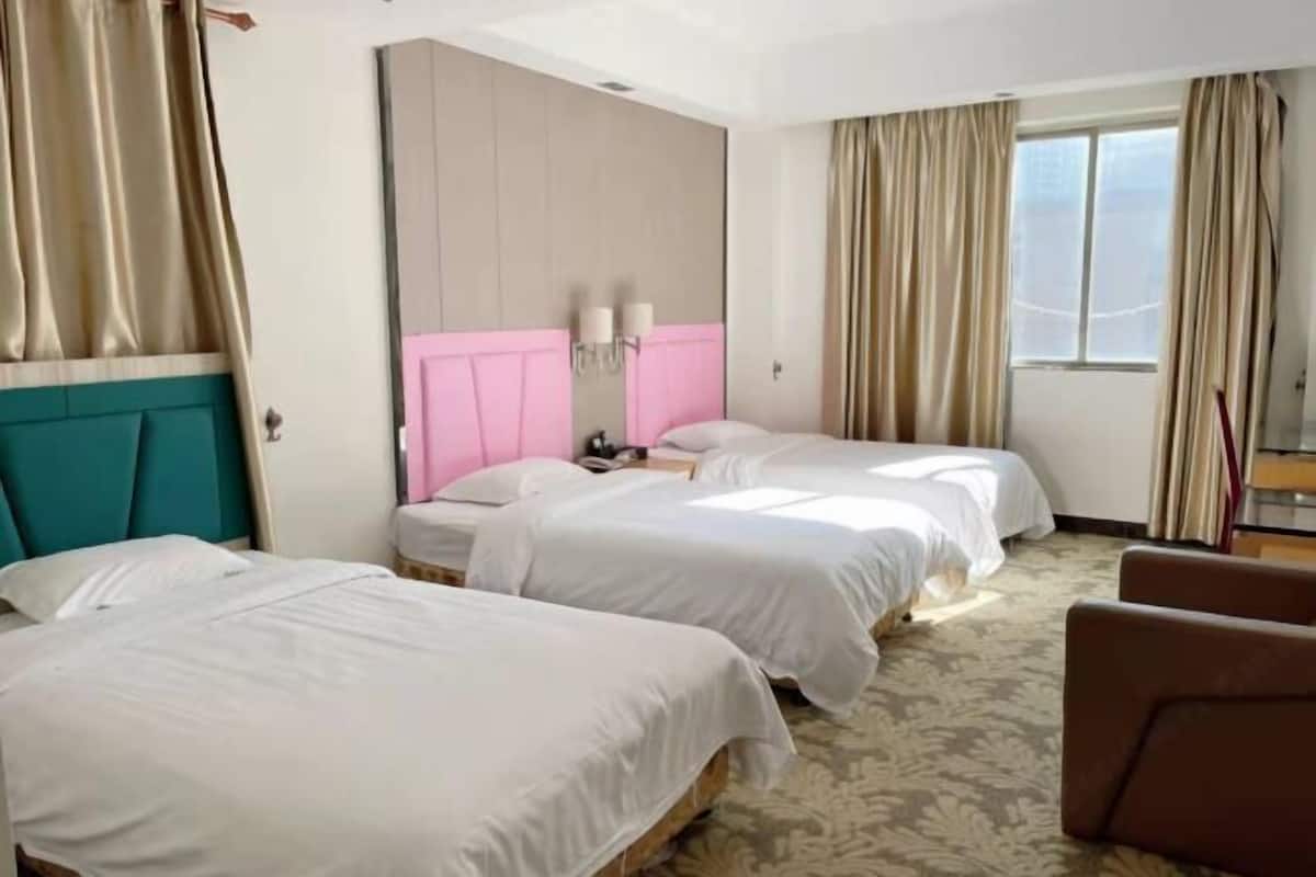 A hotel room with two beds, a large window with curtains, a pink headboard, and a teal accent wall.