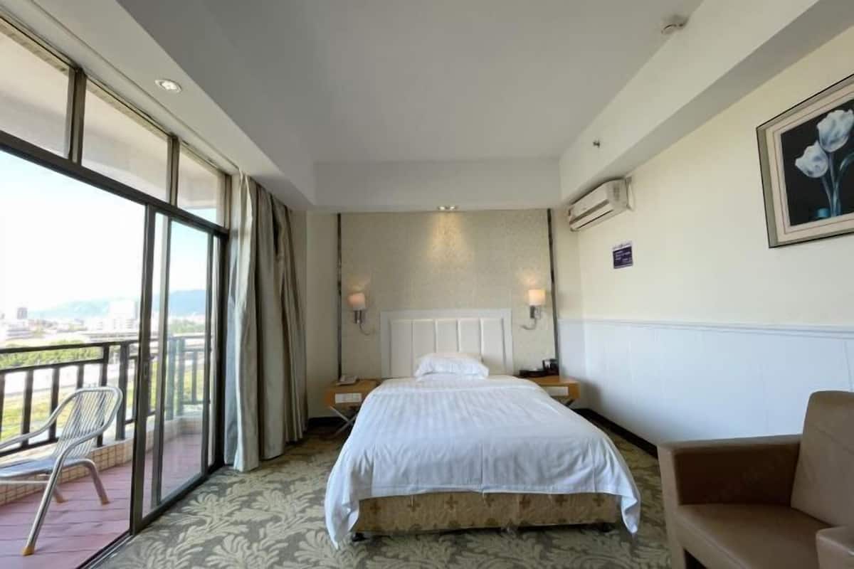 A hotel room with a large bed, a balcony with a chair, and a view of the city.