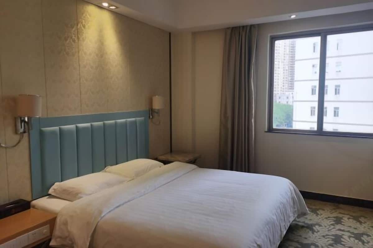 A hotel room with a large bed, a bedside table, a lamp, and a window with curtains.