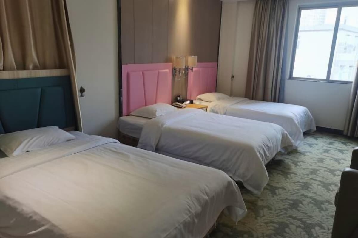 A hotel room with two beds, a pink headboard, a nightstand with a lamp, and a window with curtains.