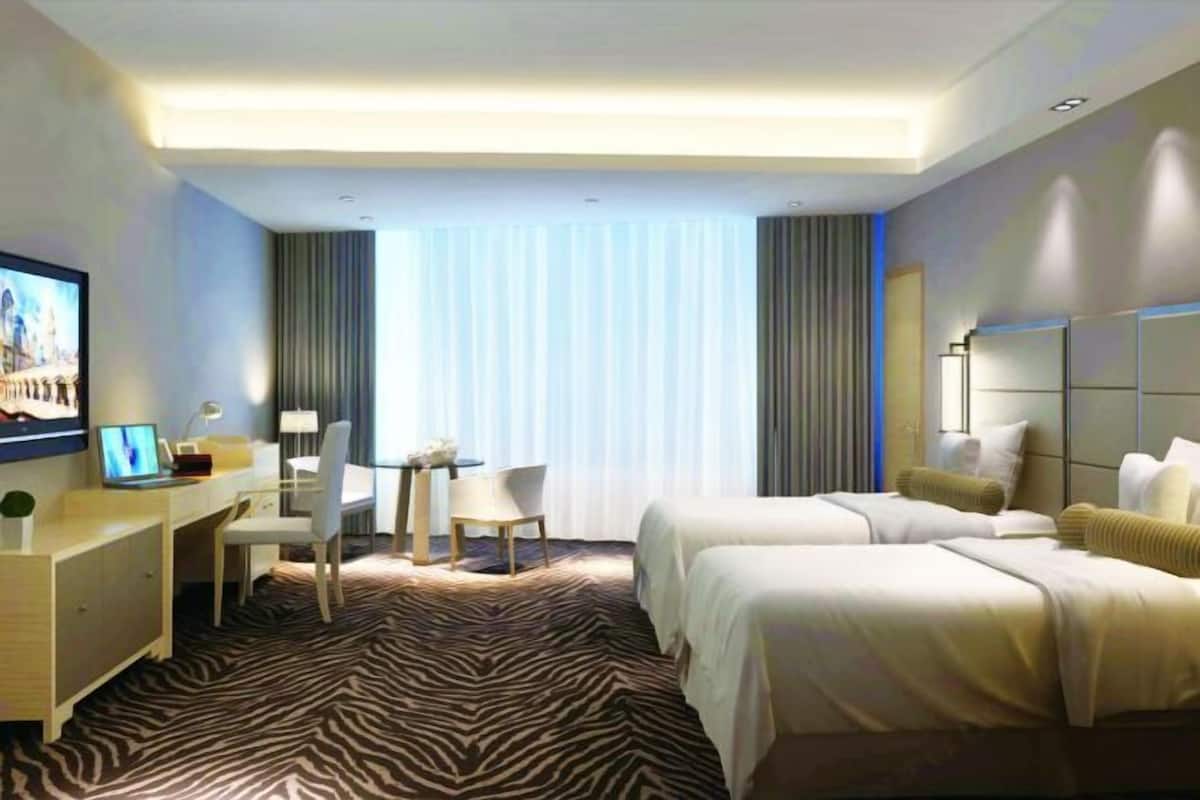 A hotel room with two beds, a desk with a chair, a TV, and a zebra-patterned carpet.