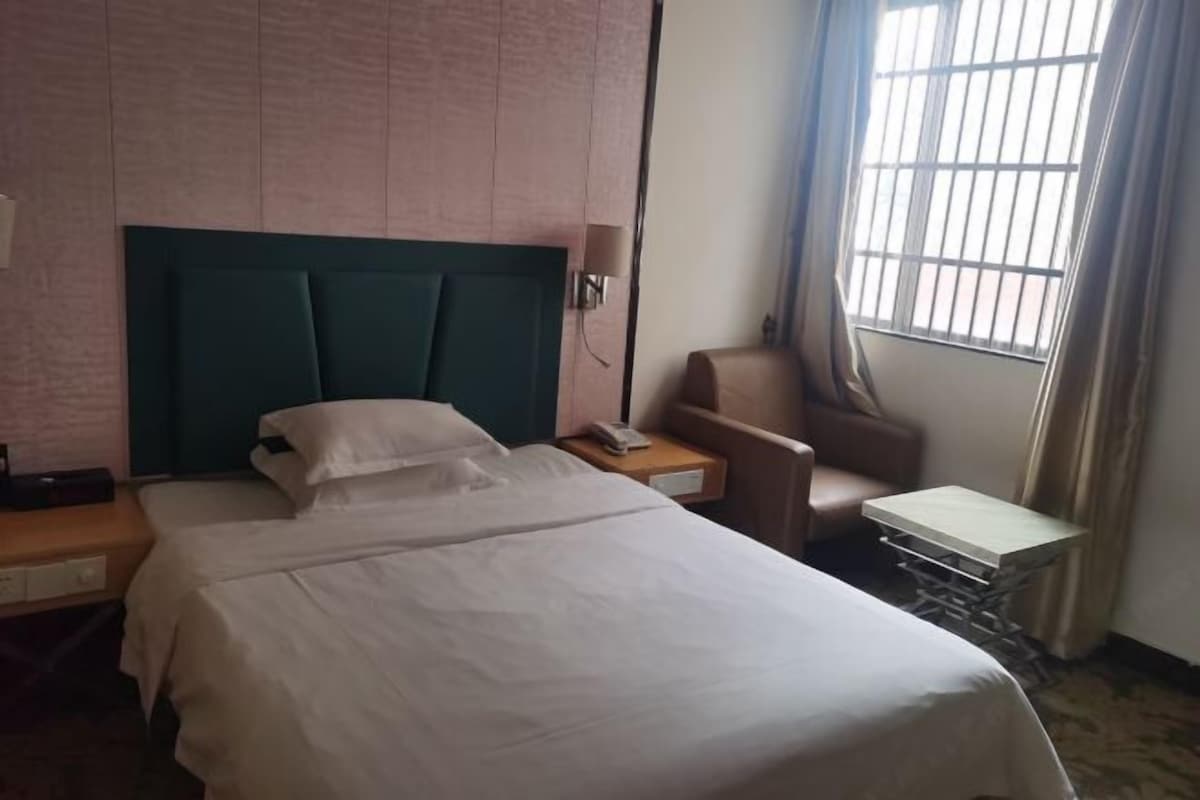 A hotel room with a large bed, a bedside table with a lamp, a chair, and a small table.