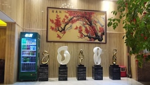 A lobby with a vending machine, a painting of a tree, and abstract sculptures on pedestals. - Jufu Hotel (Enping)