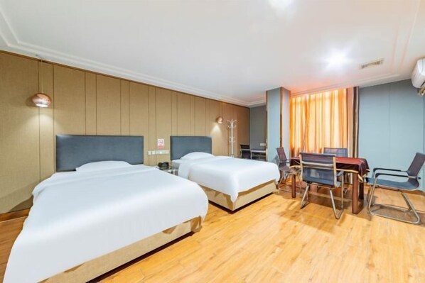 A hotel room with two beds, a desk, a chair, and a lamp.