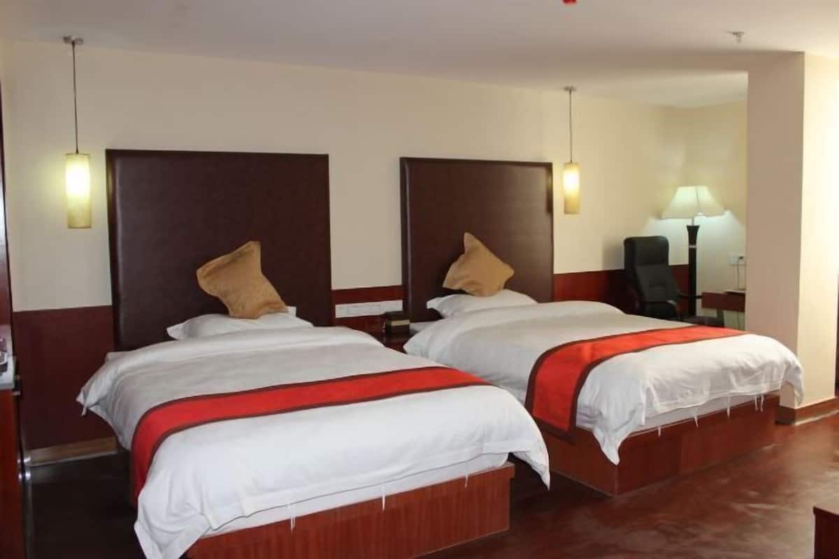 Una habitación de hotel con dos camas, cabeceros de madera, lámparas de noche y mesitas.