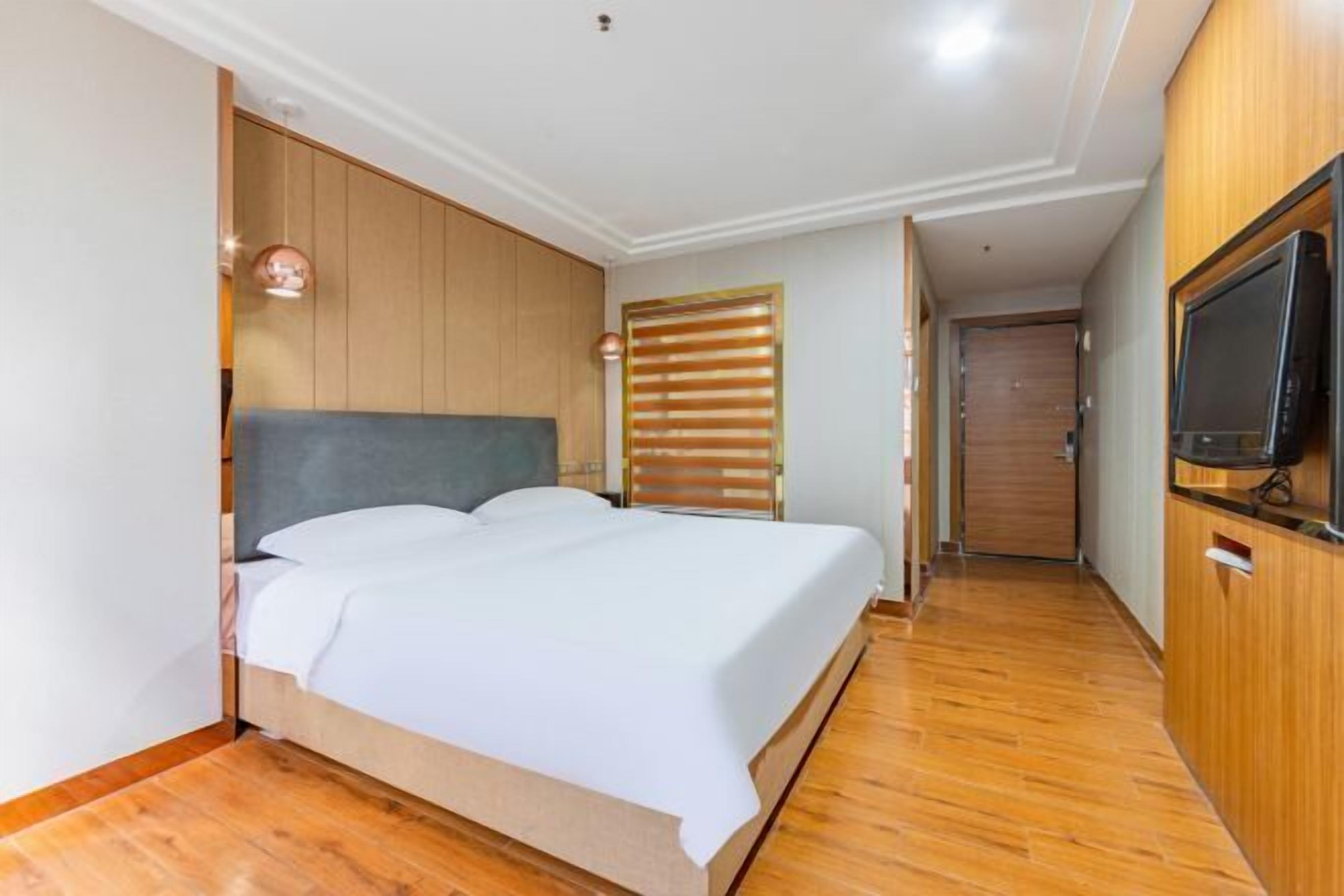 A bedroom with a wooden headboard, a bed with white linens, a television on a wooden cabinet, and a wooden floor.