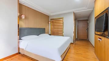 A bedroom with a wooden headboard, a bed with white linens, a television on a wooden cabinet, and a wooden floor.