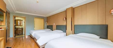 A hotel room with three beds, wooden flooring, and a kitchenette in the background.
