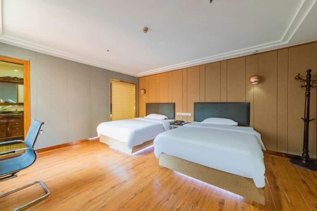 Una habitación de hotel con dos camas, una silla, suelo de madera, un espejo y una puerta.