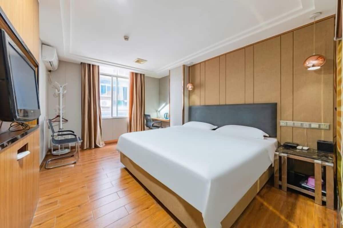 Una habitación de hotel con una cama grande, televisión, escritorio y una silla.