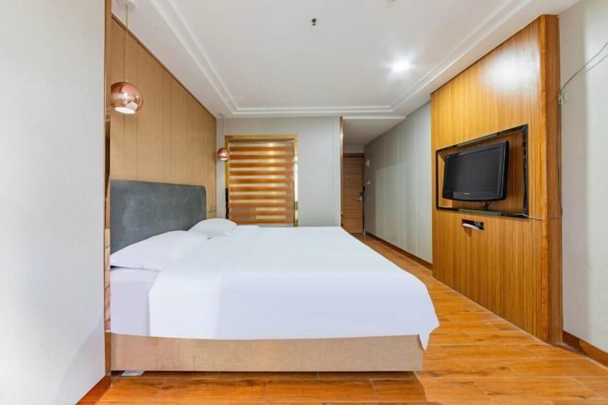A bedroom with a bed, wooden paneling, a television, and a ceiling light.